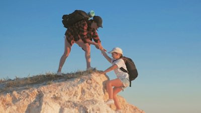 A person at the top of a hill reaches down to help a friend to reach the top too.