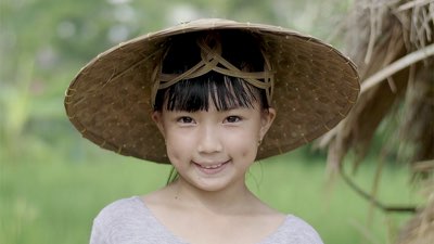 A smiling young Asian girl wearing large brim hat
